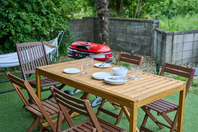 芝生の庭に置かれたウッドテーブルとBBQコンロ